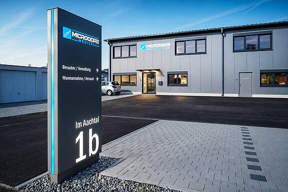 Werbeanlage mit beleuchtetem Fassadenlogo und Werbepylon am Firmengebäude